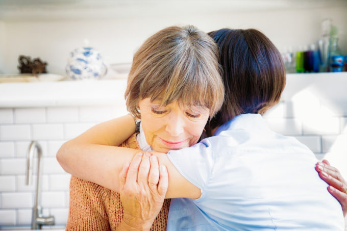 Senior mother hugs daughter while grieving, sad as she remembers her lost husband.